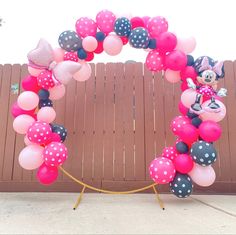 a minnie mouse balloon arch is decorated with pink, black and white balloons in front of a wooden fence