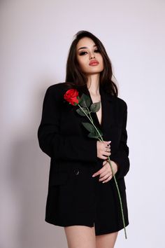 a young woman holding a rose in her right hand and wearing a black blazer