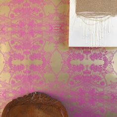 a wooden chair sitting in front of a wall with pink and gold designs on it