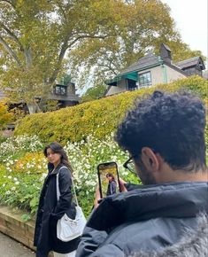 a woman taking a photo with her cell phone in front of some flowers and trees