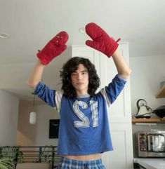 a young man with long curly hair and red mittens on his head is standing in the kitchen