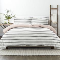 a bed with striped comforter and pillows in a white room next to a plant