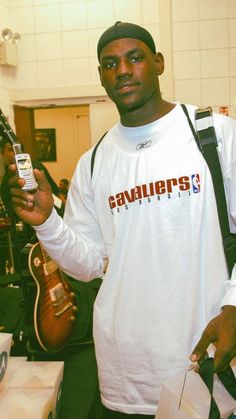 a man holding a cell phone in his right hand while standing next to a guitar