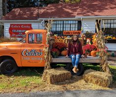 a woman sitting on a bench in front of an orange truck filled with pumpkins