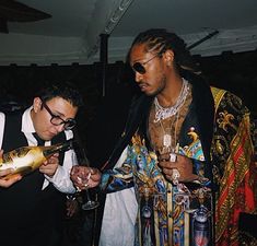 two men standing next to each other holding wine glasses and looking at something in front of them