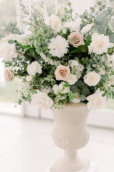 a vase filled with white flowers and greenery