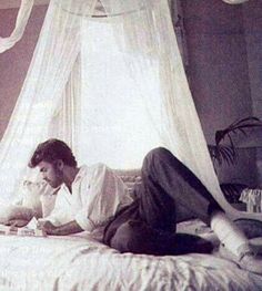 an old photo of two people laying on a bed in a room with white drapes