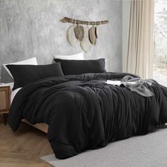 a bed with black comforter and pillows in a room next to a wall hanging with feathers