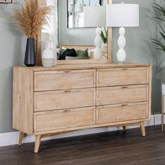 a wooden dresser sitting next to a mirror on top of a hard wood floor covered in white vases