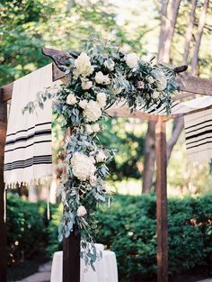 an outdoor wedding ceremony with white flowers and greenery on the arch, draped in black fabric