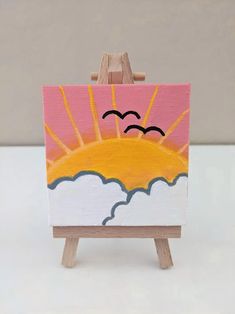 an easel with a painting on it that has a sun and clouds painted on it