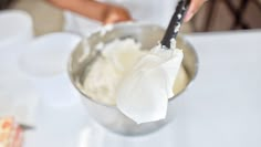 a person holding a spoon in a metal bowl filled with whipped cream and other items