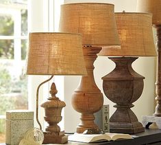 three wooden lamps sitting on top of a table next to a book and lamp shade