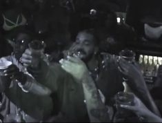 a group of people sitting at a table with drinks in their hands and one person holding a wine glass up to his mouth