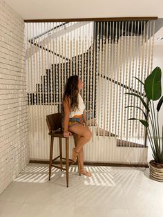 a woman sitting on a chair in front of a window with vertical blinds behind her