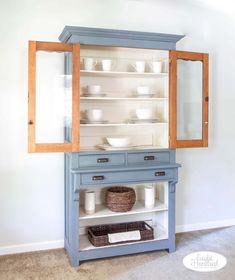 a blue china cabinet with glass doors on the top and bottom, in a white room