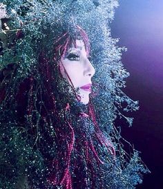 a close up of a person with long hair and glitter on her face, wearing a headdress