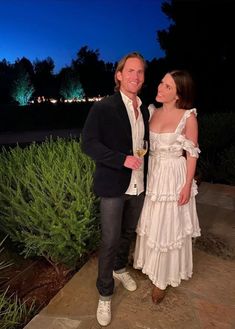 a man and woman standing next to each other in front of some bushes at night