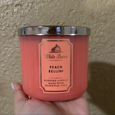 a hand holding a pink candle that says peach bellini on the front and side