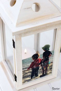 a small white lantern with two children on the beach and one is holding a candle