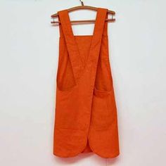 an orange vest hanging on a hanger against a white wall with clothes pins attached to it