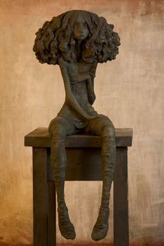 a sculpture of a woman sitting on top of a wooden chair with her hair blowing in the wind