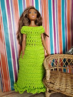 a doll wearing a green crochet dress next to a wicker chair