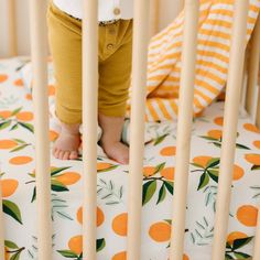 a baby standing in a crib with oranges on the bedding and sheets