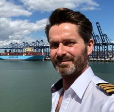 a man with a beard and uniform standing in front of a large body of water