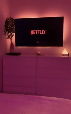 a television that is on top of a dresser next to a bed with purple sheets