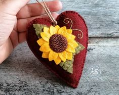 a hand holding a heart shaped ornament with a sunflower on it