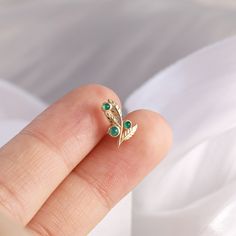 a person's hand holding a ring with two green stones on top of it