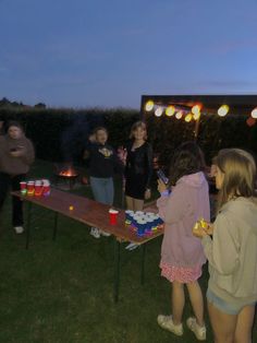 a group of people standing around a table with drinks on it and lights hanging from the ceiling