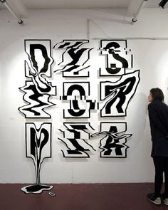 a woman standing in front of a white wall with black and white artwork on it