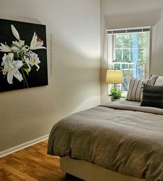 a bed sitting in a bedroom next to a window with a painting on the wall