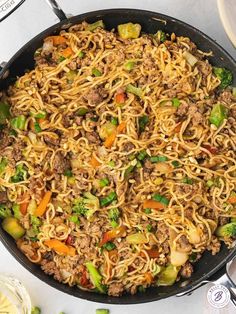 a skillet filled with noodles and vegetables on top of a white table next to utensils