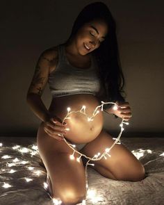 a pregnant woman sitting on top of a bed with fairy lights around her stomach and belly