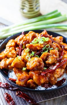 chicken with sauce and green onions in a black bowl on a wooden table next to chopsticks