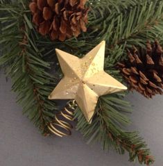 a gold star ornament hanging from a christmas tree with pine cones on it