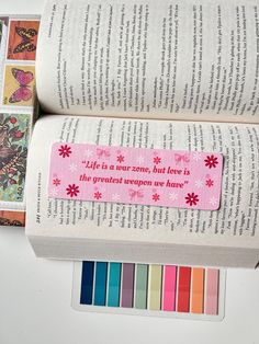 an open book with a pink ribbon on it next to some colored crayons