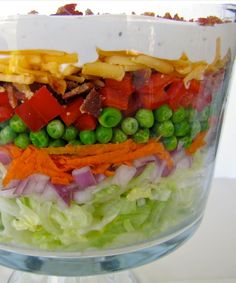 a salad in a glass bowl with peas, carrots, and other veggies