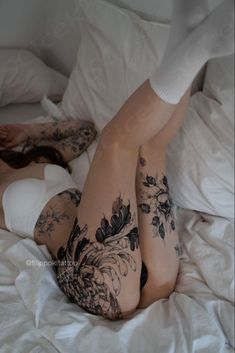 a woman laying on top of a bed covered in white sheets and pillows with tattoos on her legs