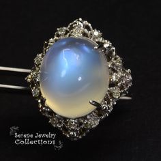 This large rare Moonstone Cabochon Ring is set in 14k solid gold and exhibits mesmerizing blue flash aduralescence. Scintillating diamonds surround this natural beauty! Ring Size: 5.75 Total Weight: 13.65 grams Precious Metal: 14k solid gold Precious stones: -Moonstone Center Stone: 18.5mm x 16.2mm, 23.05 carats -White Round Diamond: 0.4ct Elegant Collectible Moonstone Ring, Fine Jewelry White Gold Moonstone Cabochon Ring, Celestial Round Moonstone Ring For Formal Occasions, Celestial Moonstone Ring For Formal Occasions, Unique Oval Moonstone Ring For Formal Occasions, Formal Jewelry With Center Stone In Moonstone, Unique Moonstone Gemstone Ring For Formal Events, Unique Moonstone Gemstone Ring For Formal Occasions, Elegant Moonstone Gemstones For Anniversary