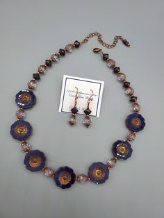 This necklace and earring set is very beautiful and one of my favorites of all time.  All beads used are glass and manufactured in the Czech Republic.  The hibiscus flowers are purple silk with an antique copper wash.  Setting off those flowers and adding the sparkle, are table cut crystal spiral faceted beads that have a purple copper effect applied.  Pretty purple and copper "Saturn" beads are the perfect touch to finish out the beauty of this necklace.  I love Czech glass beads because of their quality and precision. Necklace length is 17" and a 3" extender antique copper chain is attached so you can adjust necklace to your neckline.  Photos show short and extended lengths.  Earrings are 1 and 5/8" long and are finished with 100% Copper hook wires. Gold Glass Flower Jewelry, Gold Flower-shaped Glass Jewelry, Gold Glass Flower Shaped Jewelry, Elegant Glass Flower Necklaces, Elegant Flower Shaped Glass Necklaces, Gift Jewelry With Flower Charm And Czech Glass, Gift Jewelry With Flower Charm In Czech Glass, Elegant Flower-shaped Glass Necklaces, Elegant Glass Flower Necklace