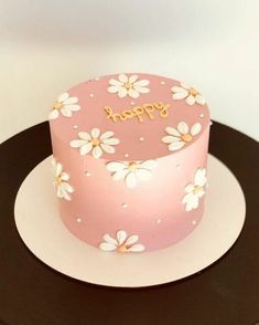 a pink birthday cake with white flowers and the words happy written on it in gold lettering