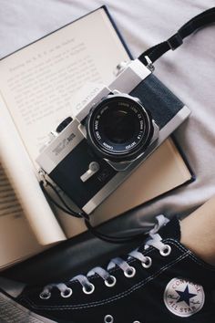 an open book, camera and converse sneakers on a bed