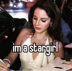 a woman sitting at a table writing on a piece of paper with the words i'm a stargirl