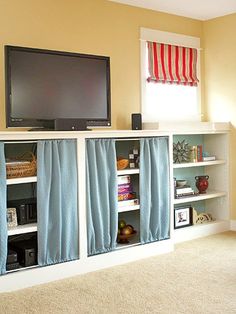 a flat screen tv sitting on top of a white book shelf next to a window