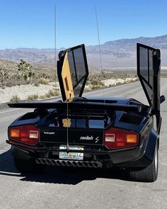 the back end of a black sports car with its doors open on an empty road