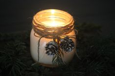 a mason jar filled with pine cones and twine on top of evergreen branches in the dark